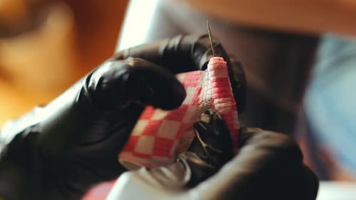 Mãos enluvadas de tatuador preparando agulha no salão