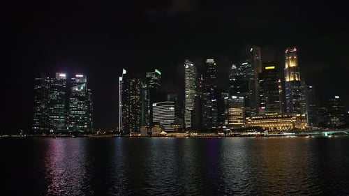 Singapore skyline casts lights against water in bay from skyscrapers at night