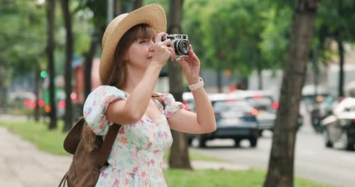 Young Woman in Floral Dress and Straw Hat Photographing Urban Street
