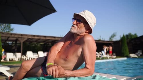 80 Years Old White Man with Beard Relaxing Near the Pool on a Hot Summer Sunny Day Lifestyle Candid