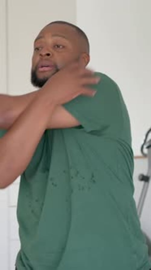 Vidéo verticale : homme aux yeux ouverts, balançant les bras, relaxant les épaules dans une pièce lumineuse, vêtu d'un t-shirt vert