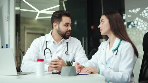 Male Head Doctor and Female Intern Sitting at Clinic Cabinet and Talking
