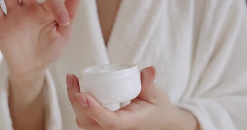 Woman Applies Cream in White Jar at Home