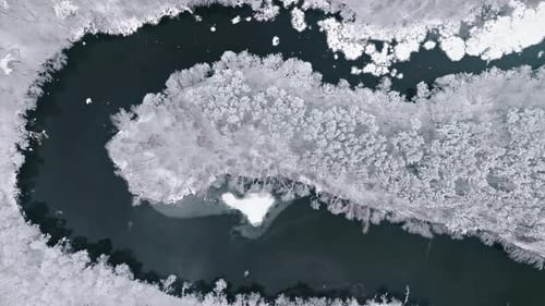 Flying above river flowing in snow-covered forest in winter, Poland.