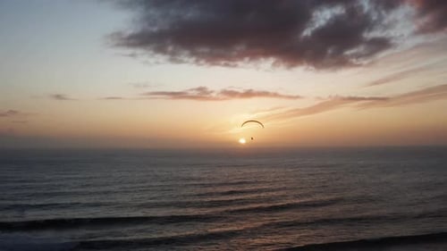 Alone paraglider flying against the colorful sunset sky above the sea. Extreme sports and adventure