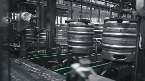 Barriles de metal moviéndose sobre una cinta transportadora en una cervecería