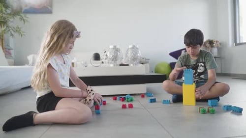 Little Girl And Boy Playing With Building Blocks Together On Living Room Floor