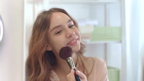 Smiling Woman Applies Makeup with Brush in Bathroom