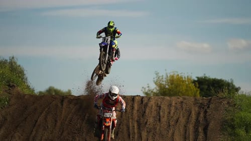 Skilled motocross riders on dirt track jumping over hill, moto competition, slow motion