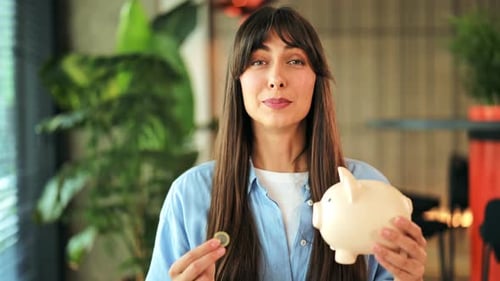 Smiling Young Woman Happily Saves Money Placing Coin Into Her Pink Piggy Bank