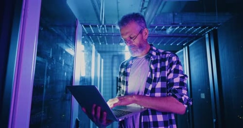 IT Professional Using Laptop in Neonlit Server Room