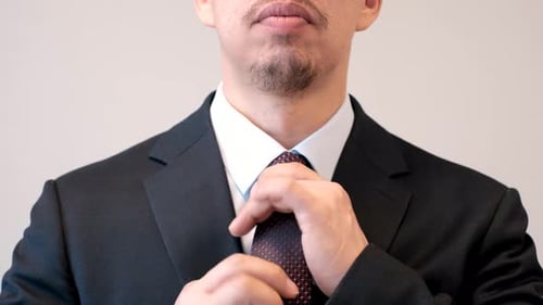 A man in a business suit corrects a tie on the shirt close-up on gray background, front view.
