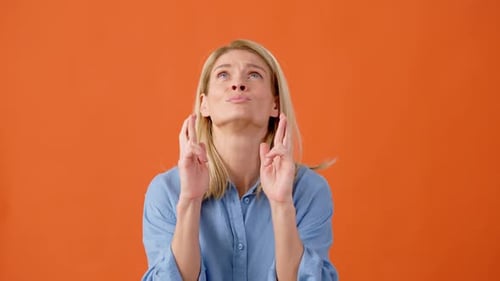 Woman Begs With Fingers Crossed on Orange Background