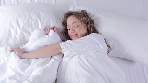 Woman Relaxes in Bed with White Linens