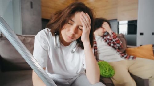 Retrato de una mujer cansada sentada en el sofá con un trapeador después de limpiar mientras su marido se ve triste