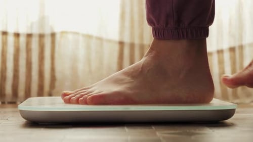 Frauenfüße stehen auf einer Waage, Frau überprüft den BMI beim Abnehmen. Messung des Körperfettübergewichts.
