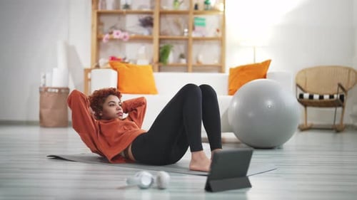 Woman Lying on Exercise Mat at Home and Doing Abs Watching Fitness Online Video on Digital Tablet