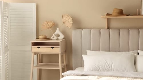 Comfortable bed with clean linens and bedside table in room. Camera moving right