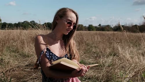 Young woman is reading a book in a meadow.