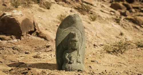 Une ancienne sculpture en pierre représentant une divinité découverte dans un paysage aride près de ruines