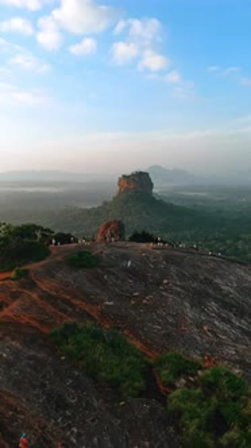 À distance du rocher de Pidurangala avec des passants. La forteresse rocheuse de Sigiriya en toile de fond.