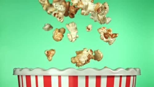 Caramel popcorn falls into striped bowl on green