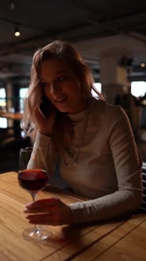 Vertical Portrait of Beautiful Blonde Young Woman Sitting in Restaurant Alone Talking on Mobile