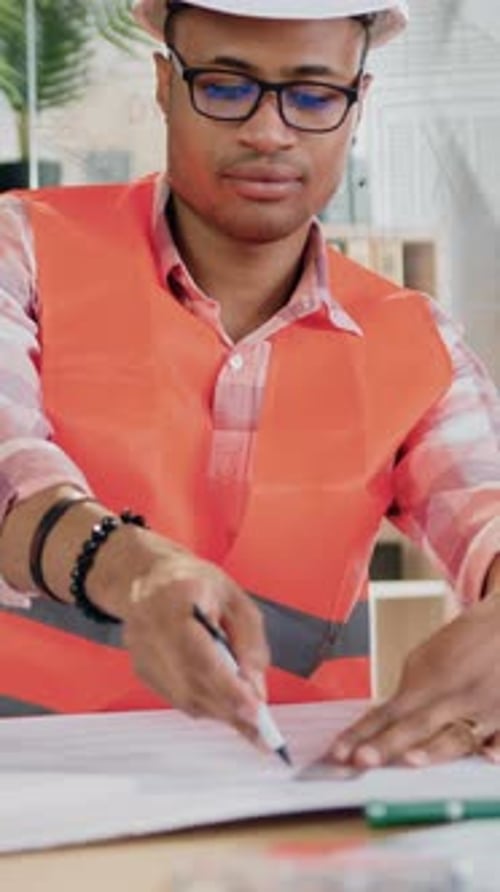 Man with Hard Hat Drawing on Blueprint in Office