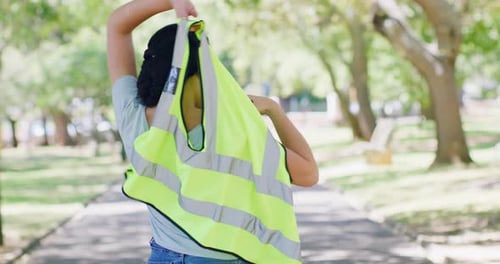 Vista trasera de una mujer que se pone un chaleco de seguridad reflectante que representa la autoridad mientras está de pie