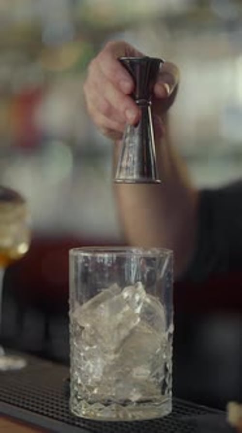 Le barman mesure les ingrédients du cocktail dans un doseur et les place dans un verre rempli de glace.