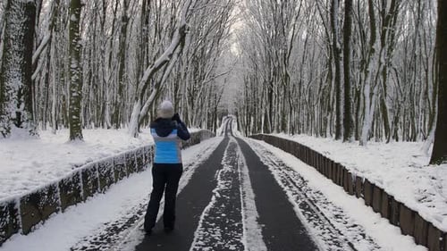 A Woman Takes Pictures of Winter Trees with Snow and the Road She is Walking on