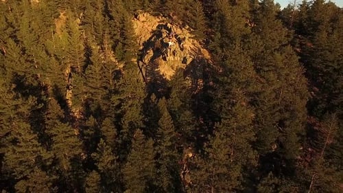 Pan out aerial shot of a people sitting on an isolated rocky outcrop on top of a forest mountain dur