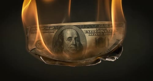 Burning dollar bill with flames on dark background.