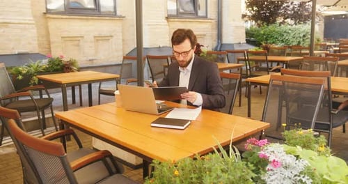 Businessman Sits and Analyses Documents in Outdoor Cafe