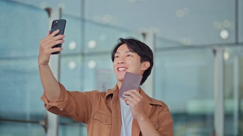 Happy asian tourist man taking selfie with passport and tickets at airport terminal