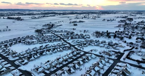 Suburban homes and rural farm fields in winter snow at colorful sunset. Aerial in USA. Modern reside