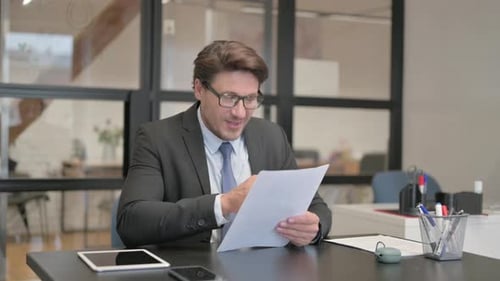 Middle Aged Businessman Cheering while Reading Documents in Office