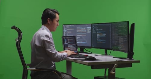Man Developer Working With Tablet While Write Code With Multiple Computer Screens In Green Screen