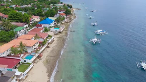 Luftaufnahme einer Küstenstadt mit bunten Häusern entlang eines Sandstrandes und Auslegerbooten auf dem