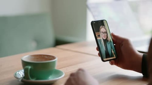 Mann ruht sich im Café aus und schaut sich den Online-Stream einer Business-Blogger-Frau auf seinem Smartphone an