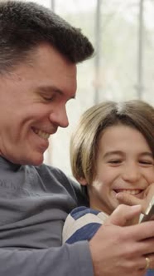 Dad and Boy Laughing at Phone Indoors