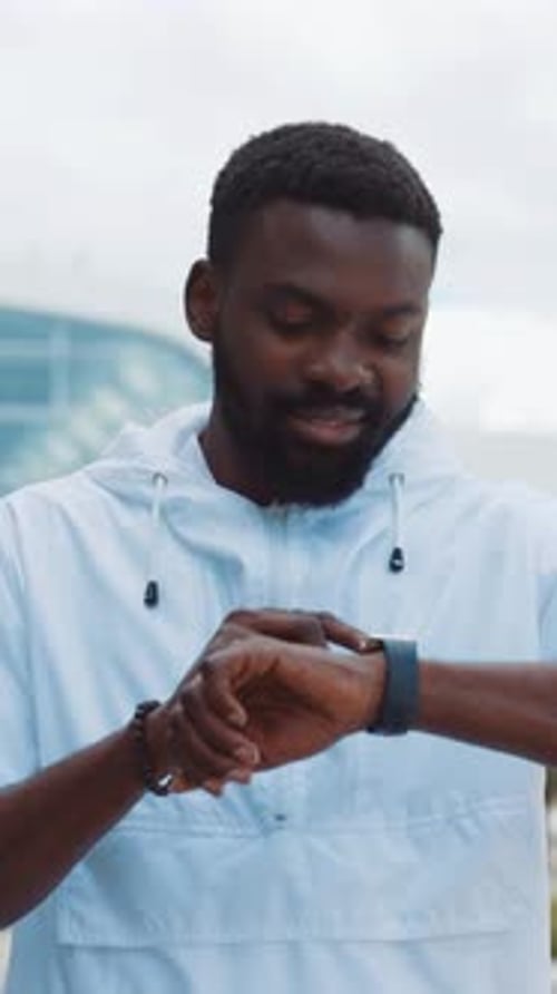 A Man is Checking His Smartwatch While Standing Outside a Sleek Modern Building Design