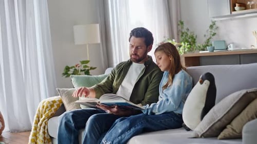Father and Daughter Reading Book Together on Couch