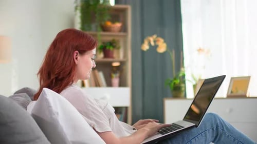 Woman Works on Laptop Reclining on Gray Sofa