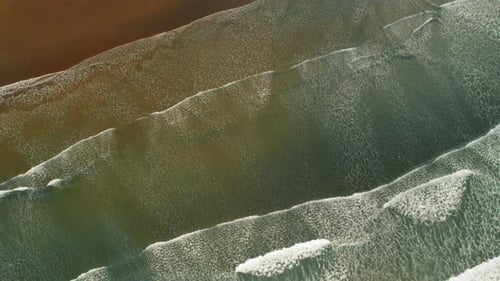 Aerial view of Pacific ocean waves forming textures on tropical sandy beach
