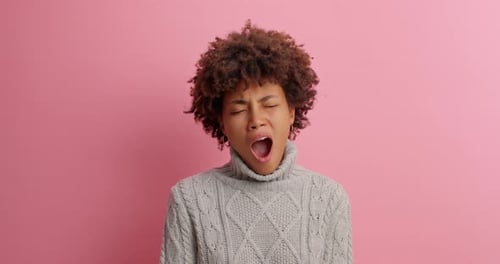 Young Woman Yawning Against Pink Background