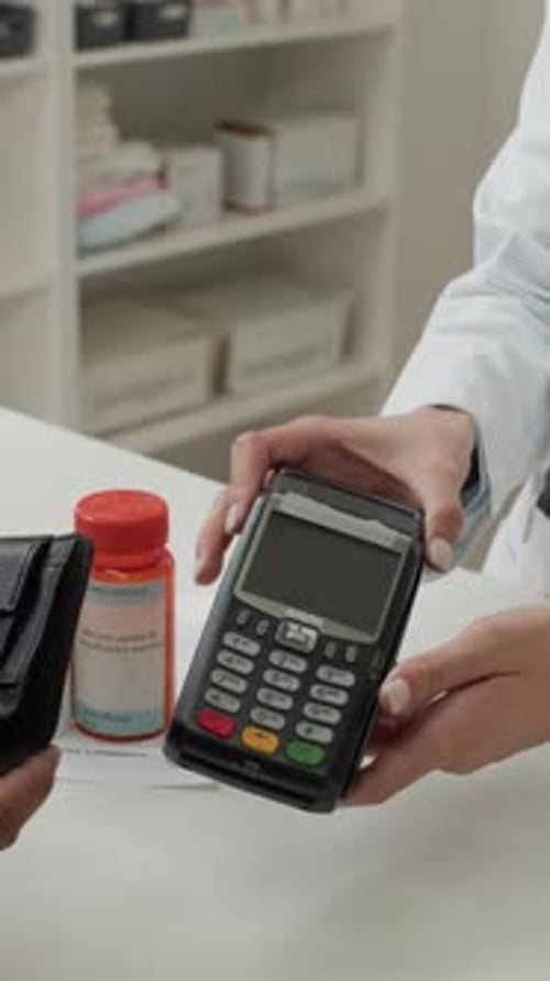 Female Pharmacist Handing Payment Terminal to Customer Vertical