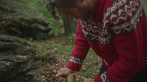 Man Splitting Wood with Hatchet to Make Campfire in Forest