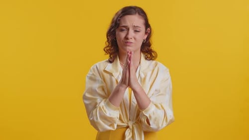 Young Woman Praying and Gesturing on Yellow Background