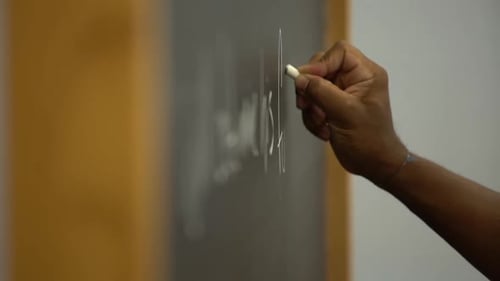 Hand Writes on Chalkboard with White Chalk
